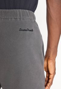 Gray sweatpants featuring an elastic waistband, side pockets, and embroidered "SnowPeak" logo near the back pocket. Smooth texture.