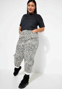 Camisa gráfica negra con el texto "INTENSE"; pantalones de tiro alto beige con estampado animal negro; zapatillas negras con los puños doblados.