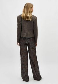 Blazer din tweed maroniu personalizat, cu padded shoulders, asortat cu pantaloni largi din mărgele în tonuri închise. Textură netedă cu un luciu subtil.