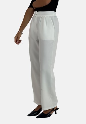 Pantalons blancs ajustés avec des plis, une texture lisse et une taille haute. Associés à des escarpins noirs à bout pointu.