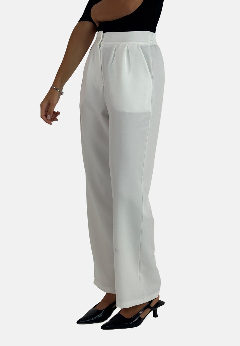 Witte maatwerk broek met plooien, een gladde textuur en een hoge taille. Gecombineerd met zwarte puntige hakken.