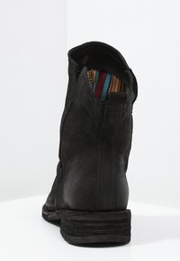 Botín de tobillo de cuero perforado negro con un tacón apilado y forro de tela a rayas multicolores visible en el interior.