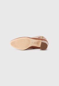 Pantofii din piele de culoare tan au un toc mic și pătrat, cu o talpă texturată, și o cataramă decorativă de culoare aurie pe lateral. Au o textură netedă și un vârf ușor ascuțit.