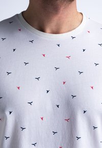 Bílý bavlněný tričko s malým, rozptýleným vzorem červených a námořnických modrých motivů, s kulatým výstřihem a měkkou texturou.