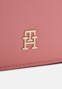 Rosa Lederhandtasche mit einem goldenen Metalllogo und gesteppten Akzenten. Die glatte Textur betont minimalistisches Design.