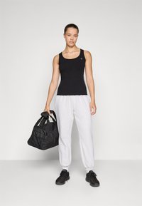 Mustmustriibuline must tank top õhukeste rihmadega, sobitatud heledate hallide dressipükstega. Mudel hoiab käes musta duffel-kotti, millel on võrkkotsection.