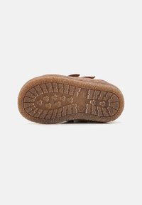 Semelle en caoutchouc brun avec un motif texturé et un profil pour une traction optimale. Bords arrondis avec une légère courbure ; présente des détails en relief pour une meilleure prise.