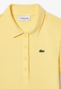 Gul ribbad pikétröja med klassisk krage, femknapprad och en grön Lacoste-krokodil-logotyp på vänster bröst.