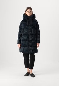 Palton pufos negru cu carouri, cu guler înalt, glugă și fermoar frontal. Asortat cu pantaloni scurți negri și pantofi slip-on.
