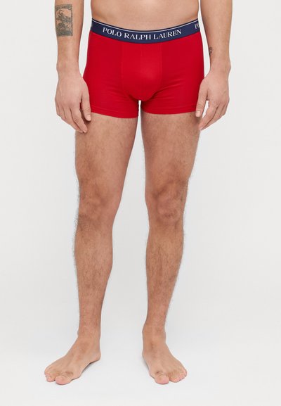 Punaiset venyvät bokserit sinisellä vyötärönauhalla, jossa on "POLO RALPH LAUREN" -logo; suunniteltu tiiviiksi istuvuudeksi ja minimaaliseen lahjepeittoon.