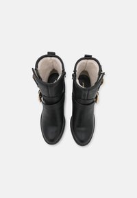 Par de botas de cuero negro hasta el tobillo con hebillas doradas y forro de lana blanca, vistas desde arriba sobre un fondo plano.