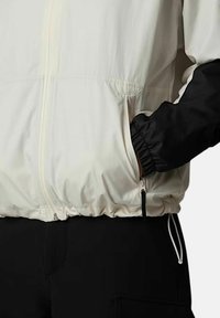 Lekka kurtka z białym korpusem i czarnymi rękawami, z zamkiem błyskawicznym, elastycznymi mankietami oraz przednią kieszenią na zamek.