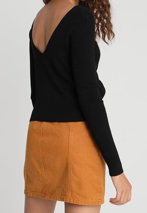 Maglione nero a costine con scollatura a V profonda sul retro, abbinato a una gonna di jeans arancione aderente con cuciture frontali e una finitura testurizzata.