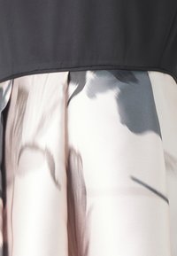 Schwarzes Oberteil, befestigt an einem plissierten Rock mit einem kontrastreichen abstrakten Blumendesign in Weiß-, Grau- und Schwarztönen.