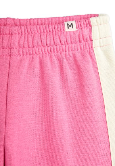 Rosa Sporthose mit einem elastischen Bund. Verfügt über einen kontrastierenden cremfarbenen Streifen an der Seite. Größenetikett mit "M" markiert. Weicher Stoff.