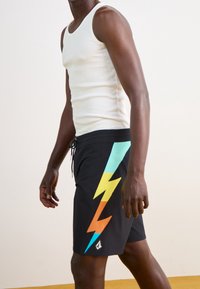 Shorts de bain noirs avec un graphique d'éclair multicolore en teal, orange et jaune, dotés d'une taille élastique et d'un cordon de serrage ajustable.