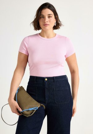 Ljusrosa ribbad kortärmad topp ihop med högmidjade mörkblå denimbyxor. Håller en grön clutch med blå detaljer.