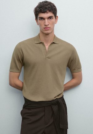 Brown short-sleeve polo shirt in a textured, knit fabric with a v-neck design. Paired with dark brown trousers and a tied waistband.