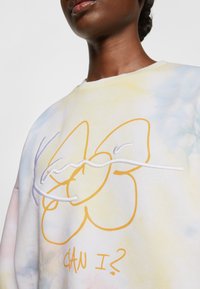 Multicolor sweatshirt met een tie-dye patroon in pastelkleuren, met gedurfde, geborduurde gele afbeeldingen van vlindervormen en tekst.