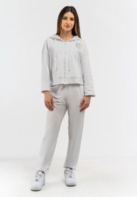 Felpa grigia chiara con zip, cappuccio, tasche frontali e design cropped, abbinata a pantaloni tapered coordinati e sneaker bianche.