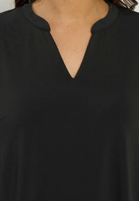 Top nero con scollatura a V e leggero colletto. Texture liscia, realizzato in tessuto morbido, privo di motivi o dettagli.