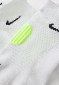 White athletic socks with black Nike logo; feature textured knit and a fluorescent green ribbed accent on the side.