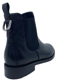 Czarny skórzany botek sięgający kostki z elastycznym panelem bocznym, pętlą do zakładania i płaską podeszwą. Gładka tekstura i minimalne szwy, zaprojektowane dla wygody zakładania.