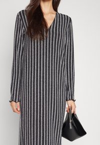 Robe rayée noire et argent scintillante avec des manches longues et un décolleté en V. Accompagnée d'un petit sac à main noir, doté d'une fermeture éclair.