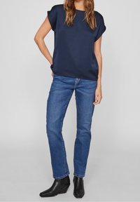 Námořnická modrá saténová halenka s krátkým rukávem a volným střihem, spárovaná se světle modrými rovnými džíny a černými botami na podpatku.