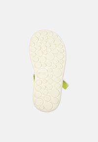 Sula av en sandal med en vit texturerad yta med cirkulära mönster, accentuerad med ett klart gult rem.