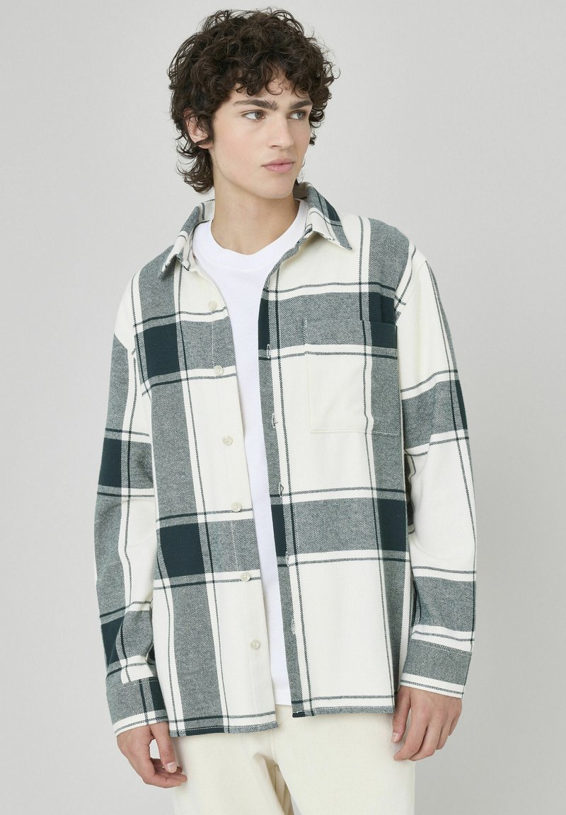 Chemise en flanelle pour homme blanche avec un motif de carreaux gris et vert foncé. Elle possède un devant à boutons, un col et une poche poitrine. Texture douce.