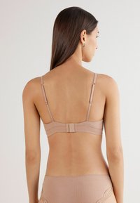 Beha in een zachte beige stof met een ribbelstructuur, verstelbare bandjes en een haak-en-oogsluiting op de rug. Geen extra versieringen.