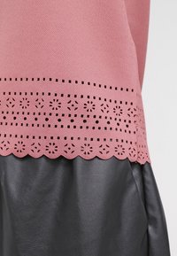 Top rosa con un tessuto texturizzato e intricati disegni a taglio lungo l'orlo, sovrapposto a un materiale simile alla pelle nera.