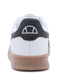 Białe sneakersy z czarnym paskiem na pięcie, teksturowaną gumową podeszwą, zaokrąglonym wzornictwem i okrągłym logo z tyłu. Klasyczna sylwetka niskiego cholewki.