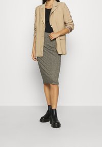 Beige kavaj över en svart topp, kombinerat med en mönstrad blyertskjol i grå nyanser och svarta ankelstövlar med kraftig sula.