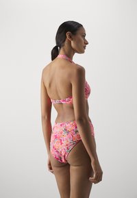 Cvjetni bikini set u vibrantnoj ružičastoj boji, s halter vratom i visokim strukom. Glatka tekstura s raznobojnim cvjetnim uzorcima.
