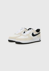 Beige and white suede sneakers with black accents, perforated toe box, white laces, and black rubber outsole. "AIR" detail on the heel.