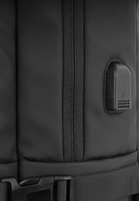 Czarny plecak z materiału, wyróżniający się teksturowanym wykończeniem, centralnym zamkiem błyskawicznym, solidnym paskiem oraz małym czarnym akcentem z metalu.