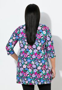 Czarna tunika w kwiaty z jaskrawymi różowymi, fioletowymi i niebieskimi kwiatami. Rękawy do łokcia, boczne rozcięcia i luźny krój.