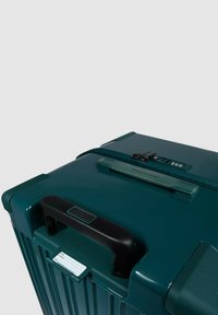 Maleta rígida color verde azulado con ranuras verticales, asa negra, cerradura de combinación y portatarjetas, con acabado liso y bordes duraderos.