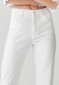 Jean blanc taille haute en denim, avec fermeture par bouton, cinq poches et coupe droite avec une texture lisse.