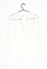 Vitt stickat tröja med ett texturerat mönster, med v-ringning och ribbade manschetter. Hänger från en svart krok mot en vit bakgrund.