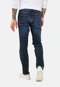 Ciemnoniebieskie dżinsy o slim fit, z kontrastującym pomarańczowym przeszyciem, pięcioma kieszeniami oraz subtelnymi detalami na tylnej kieszeni.