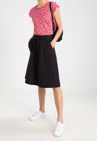 Lyserød blomsterkortærmet skjorte, sort midi nederdel med snoretræk i taljen og lommer, båret med hvide sneakers. Simpelt, afslappet outfit.
