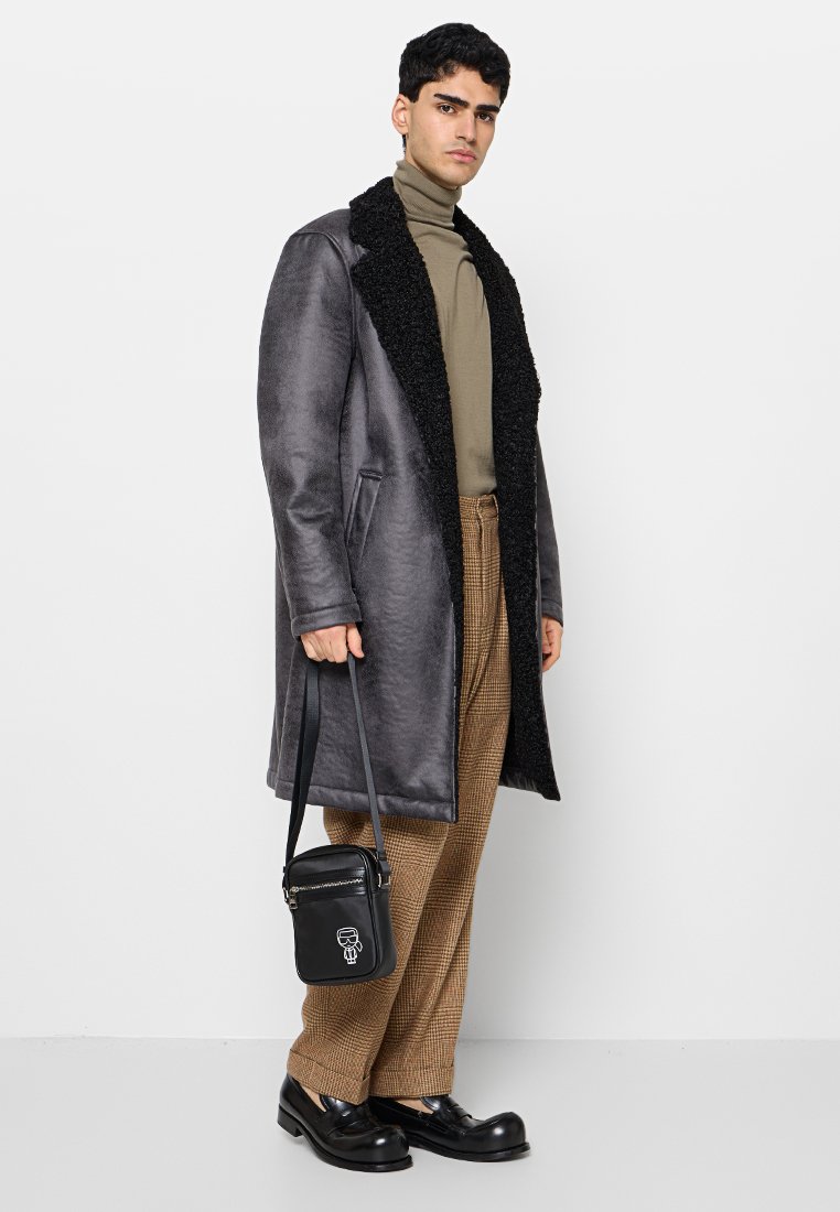Abrigo gris con cuello de piel negra, combinado con un cuello alto beige y pantalones de cuadros. Bolso bandolera negro y zapatos gruesos.