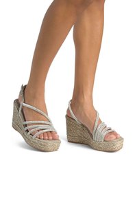 Sandali con zeppa con suola in juta intrecciata, cinturini incrociati argento e fibbia regolabile alla caviglia. Design open-toe che rivela le dita dei piedi.