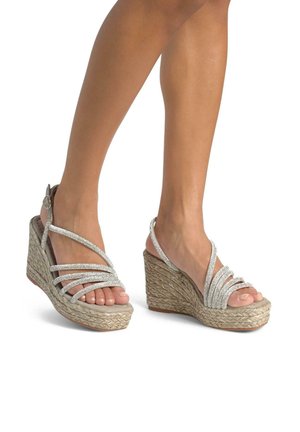 Sandali con zeppa con suola in juta intrecciata, cinturini incrociati argento e fibbia regolabile alla caviglia. Design open-toe che rivela le dita dei piedi.