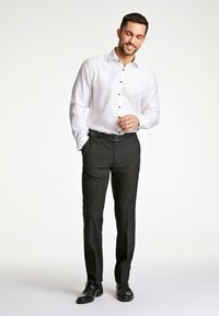 Witte button-up shirt met zwarte knopen, gecombineerd met zwarte broek en zwarte schoenen. Gladde stof en een getailleerde pasvorm.