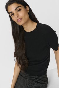 Sort kortærmet striktop med rund halsudskæring, der har en glat tekstur og tætsiddende design. Båret med et mønstret blyantskirt.