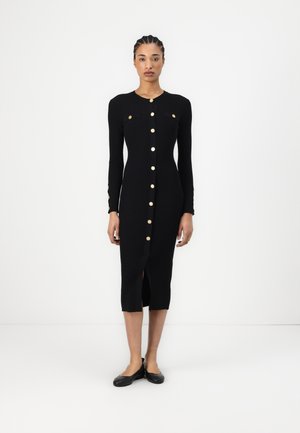 Black ribbed dress with long sleeves, gold button closures, front slit, and two chest pockets. Stitched accents on sleeves.